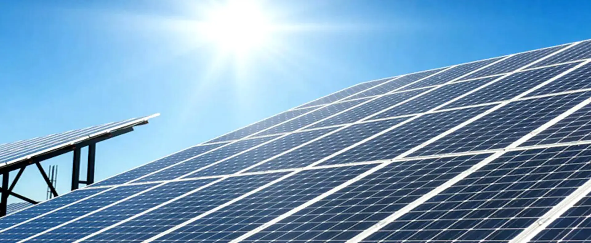 Solar panels angled towards a bright sun in a clear blue sky